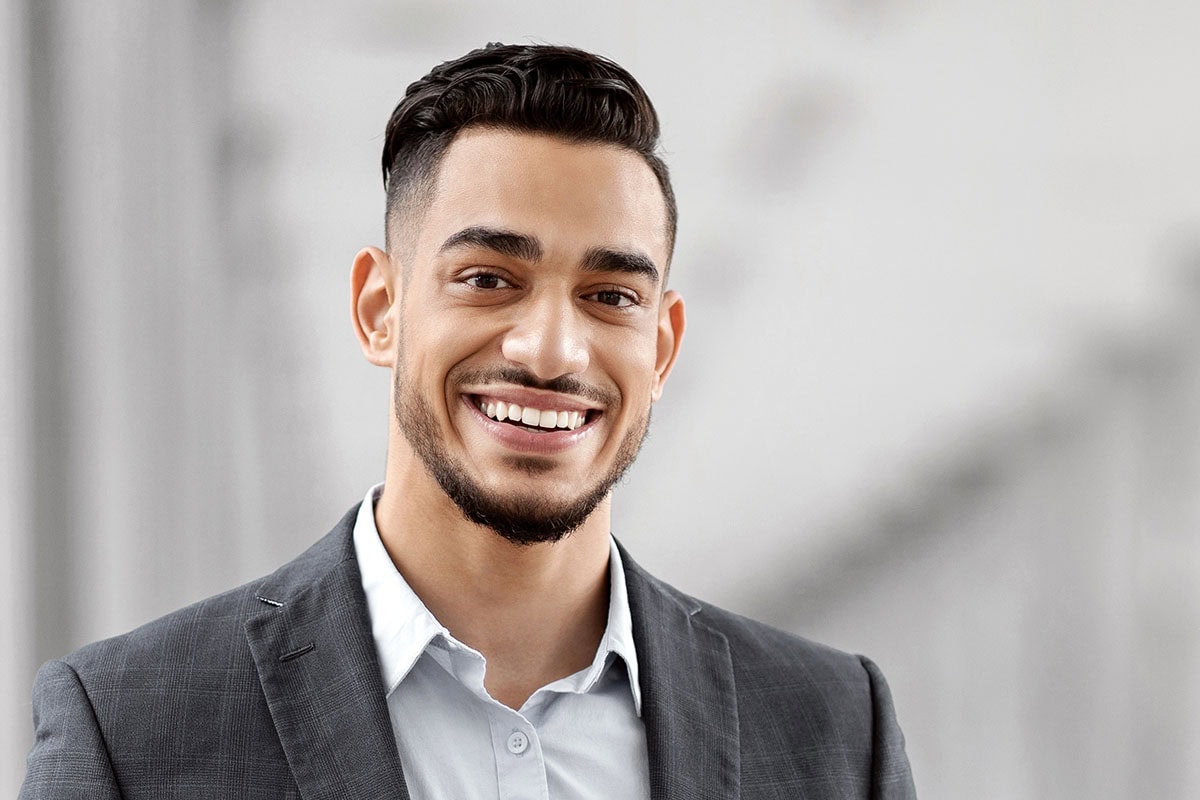Porträt eines jungen, professionell gekleideten Mannes in Anzug mit einem selbstbewussten und perfekten Lächeln.