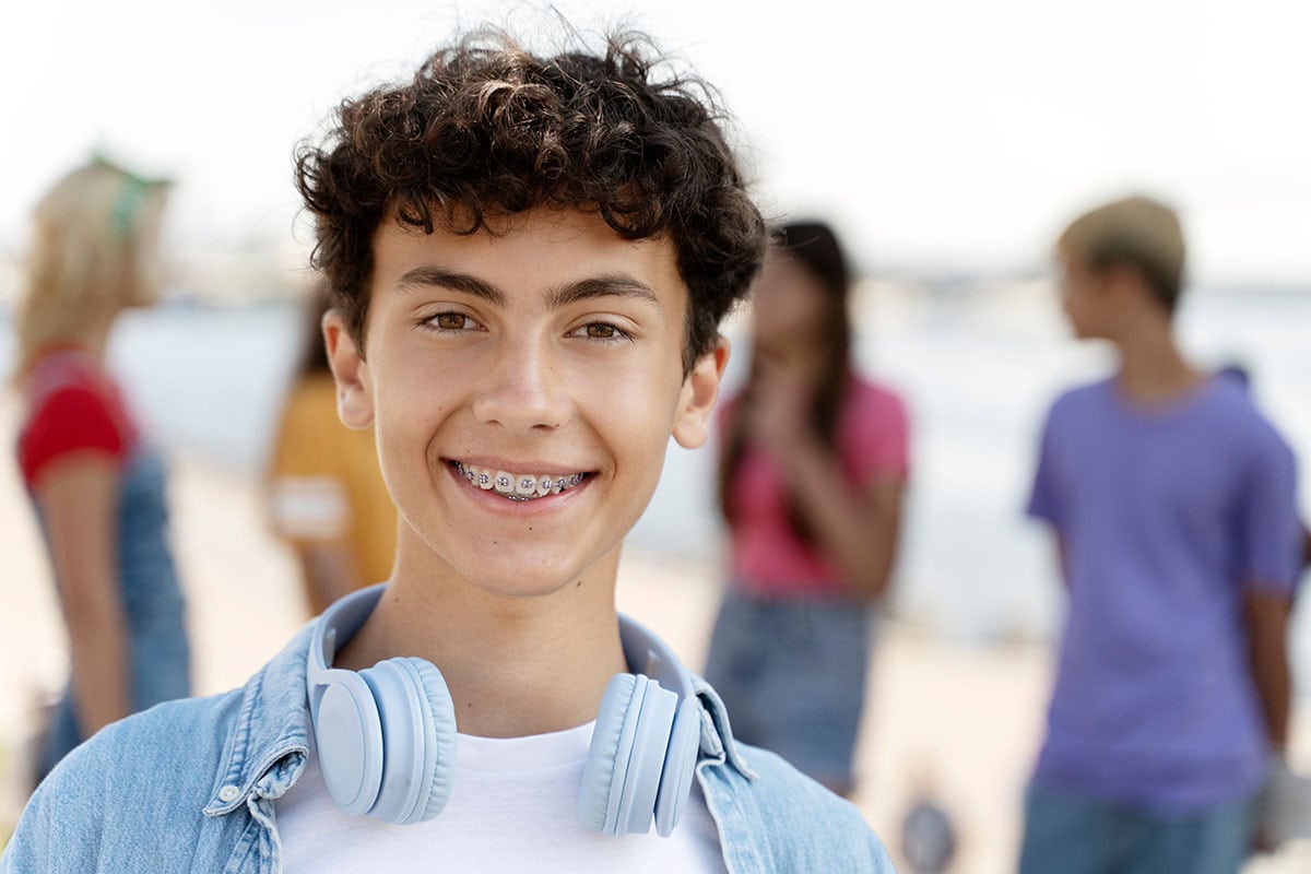 Nahaufnahme eines lächelnden Teenager-Jungen mit lockigem Haar und fester Zahnspange.