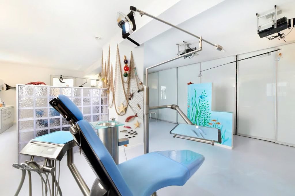 Helles Behandlungszimmer der Kieferorthopädie Dr. Beer, ausgestattet mit einem blauen Behandlungsstuhl und dekoriert mit einem maritimen Unterwasser-Thema.