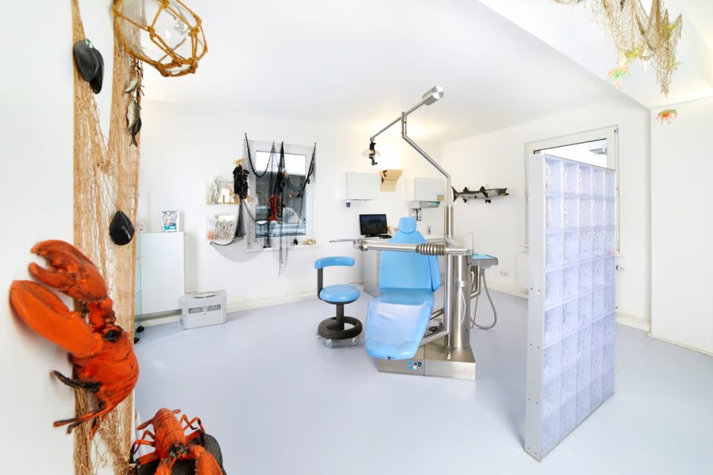 Modernes Behandlungszimmer der Kieferorthopädie Dr. Simone Beer, dekoriert im maritimen Stil mit einem blauen Behandlungsstuhl, Fischernetzen und einer Hummerfigur.