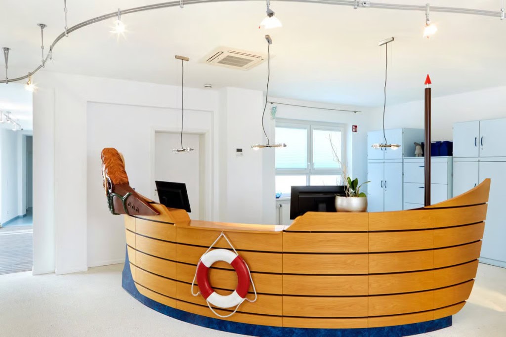 Der Empfangsbereich der Kieferorthopädie Dr. Simone Beer mit einer einzigartigen, bootförmigen Rezeptionstheke aus Holz und einem dekorativen Rettungsring.